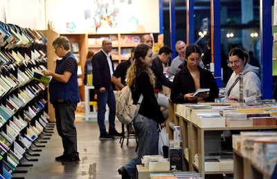 Hombres y mujeres visitan la feria, observando libros en un ambiente acogedor, con luces cálidas y estanterías repletas.