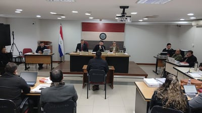 Tres miembros del panel en sala de audiencias, observando atentamente mientras un hombre, de espaldas, expresa su testimonio.