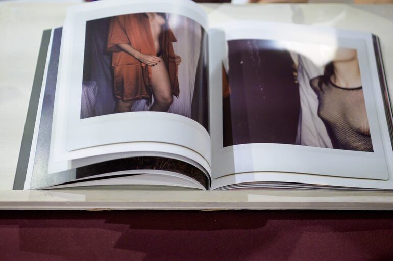 Un libro abierto con fotografías artísticas de personas, sobre una mesa de fondo claro y ambiente oscuro.