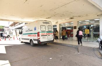 Ambulancia blanca con franjas verdes y personal médico ayudando a un paciente en un acceso urbano.