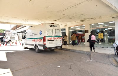 Ambulancia blanca con franjas verdes y personal médico ayudando a un paciente en un acceso urbano.