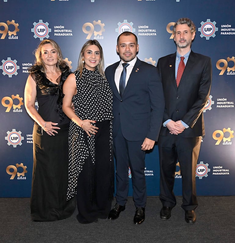 Mujeres y hombres en traje formal, sonriendo y posando frente a logotipos de UIP durante el evento de aniversario.