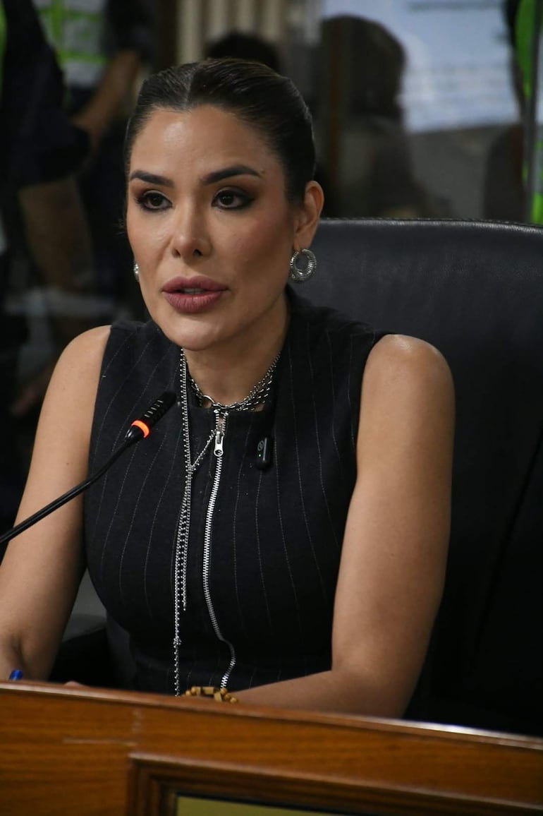 Fiorella Forestieri, con vestido negro con rayas, sostiene un micrófono y habla en un entorno formal.
