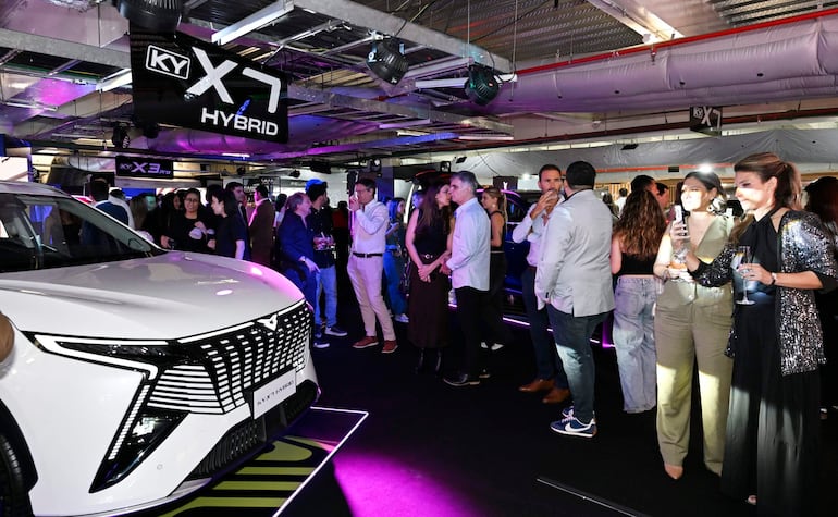 Multitud elegante en la presentación del KY X7 Hybrid, con luces de colores y banners publicitarios en un recinto moderno.