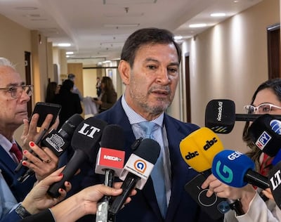 Silvio Ovelar rodeado de periodistas, con expresión seria y micrófonos de varios medios en un ambiente interno.