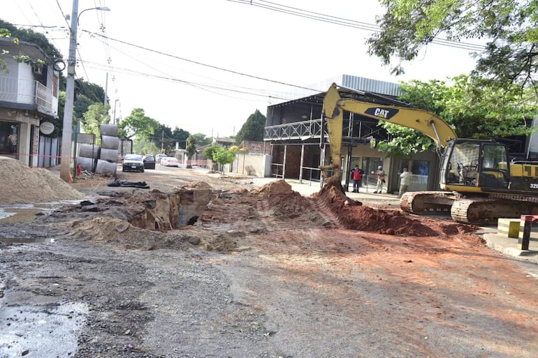 Excavadora amarilla trabaja en pozo rodeado de tierra y escombros en una calle urbana de Asunción.