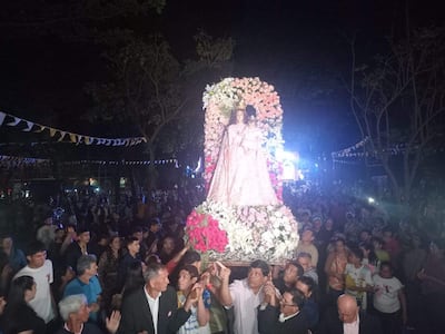 Multitud en Luque sosteniendo imagen de la Virgen del Rosario, decorada con flores, en un ambiente festivo y luminoso.