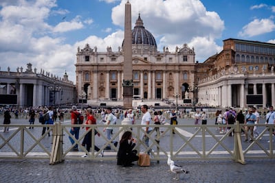 Una mujer se maquilla junto a las gaviotas y el obelisco de la Plaza de San Pedro, con la Basílica de San Pedro al fondo, en el Vaticano.