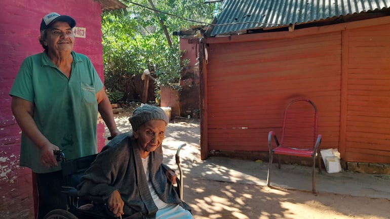 Don Miguel Mendieta empuja la silla de ruedas de su madre María Dominga León. En el fondo se nota la precaria casa de madera.