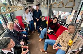 Santiago Peña, Iván Yueh-Jung Lee y otros hombres sentados en un autobús conversan, con expresión tranquila en un ambiente colorido.