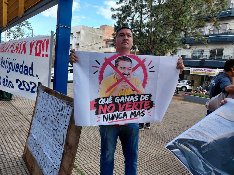 Hombre con camiseta oscura y jeans sostiene un cartel que dice 'Qué ganas de no verte nunca más' en la protesta.