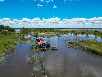 Casa de construcción precaria parcialmente sumergida en agua, rodeada de vegetación en un paisaje rural inundado.