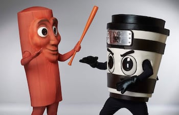 Personajes disfrazados de salchicha y vaso de café, interactuando en un set fotográfico neutral.