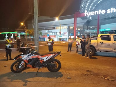 Agentes de seguridad en chalecos amarillos interactúan con una motocicleta negra y naranja mientras dos civiles observan.