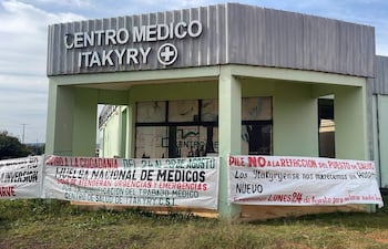 Fachada del Centro Médico Itakyry con carteles sobre huelga nacional de médicos, ambientada por un paisaje natural.