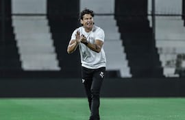 Nelson Haedo Valdez aplaudiendo, vestido con camiseta blanca y pantalones oscuros en un campo de fútbol vacío.