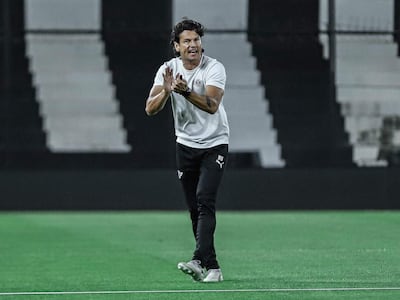 Nelson Haedo Valdez aplaudiendo, vestido con camiseta blanca y pantalones oscuros en un campo de fútbol vacío.