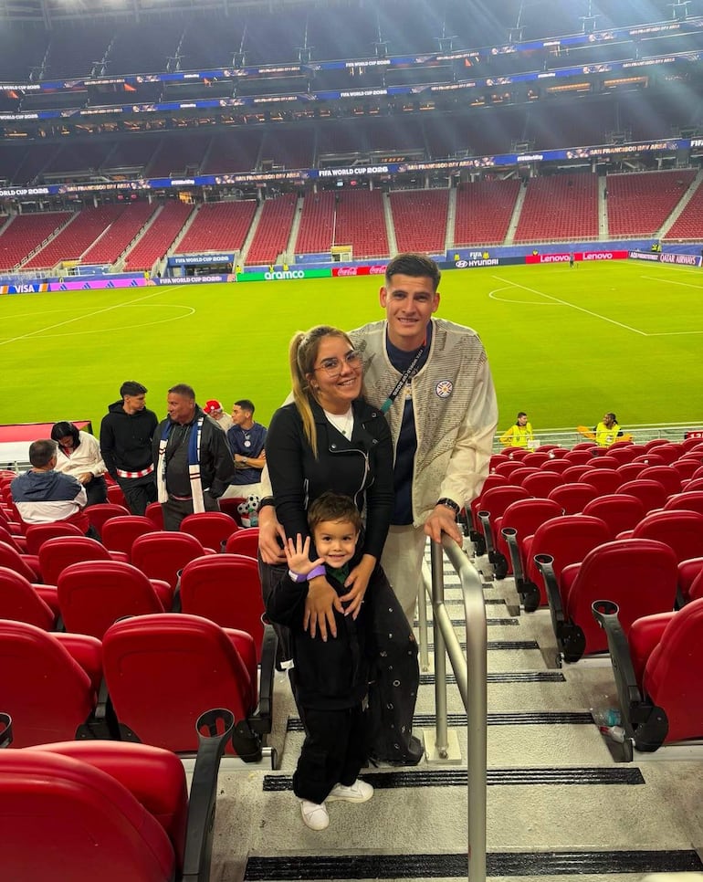 Miguel Almirón sonríe en el centro, junto a una mujer con gafas y chaqueta negra, y un niño con ropa oscura, en un estadio.
