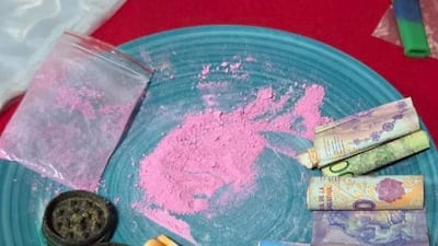 Sustancias en polvo rosa junto a billetes y un recipiente negro, evidencian actividades ilícitas en un ambiente interior.