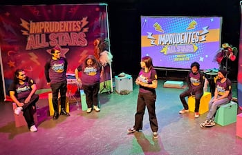 Artistas de 'Imprudentes All Stars' en un vibrante escenario; una mujer de pie se destaca mientras los demás esperan participando.