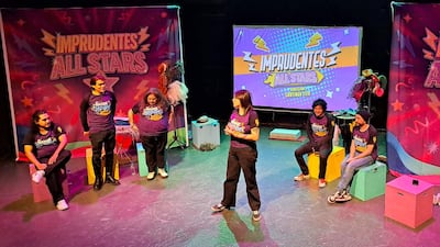 Artistas de 'Imprudentes All Stars' en un vibrante escenario; una mujer de pie se destaca mientras los demás esperan participando.