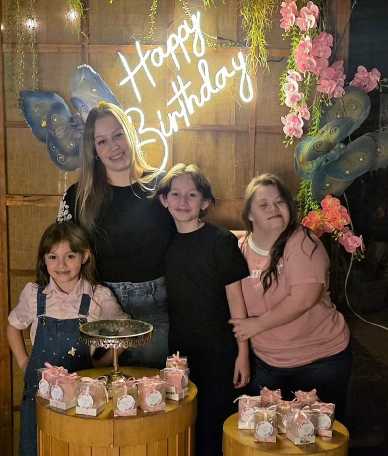 Cuatro personas sonrientes en fiesta de cumpleaños, con regalos envueltos en papel rosa y decoración festiva.