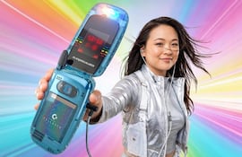 Mujer con chaqueta plateada y teléfono Commodore, sonriente, rodeada de luces coloridas en un escenario vibrante.