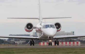 Avión de la Fuerza Aérea Paraguaya en pista, con diseño moderno en blanco y rojo, rodeado de edificios del aeropuerto.