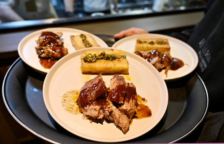 Platos con carne desmenuzada y pan, presentados en bandeja, con ambiente de cocina profesional.