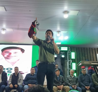 Eduardo Dejesus en pie, con micrófono y bandera, hablando mientras un grupo lo observa con atención en un ambiente decorado con luces verdes.