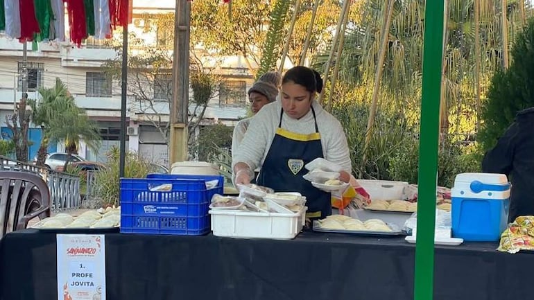 Mujer con delantal amarillo sirve platos en evento al aire libre, decorado con banderas, en un día frío.