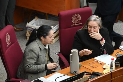 Gladys Lucía Mendoza de Esparza con abrigo claro discute, mientras Ramona Yolanda Paredes escucha atentamente en ambiente legislativo.