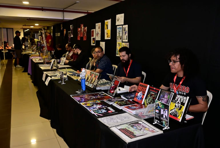 Seis personas en un stand de cómics, revisando artículos, con atención y expresiones de entusiasmo en un ambiente colorido.