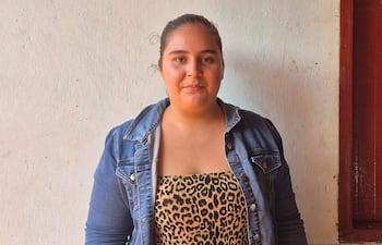 Mujer con chaqueta de mezclilla y camiseta leopardo frente a una pared blanca, con expresión neutral y cabello recogido.