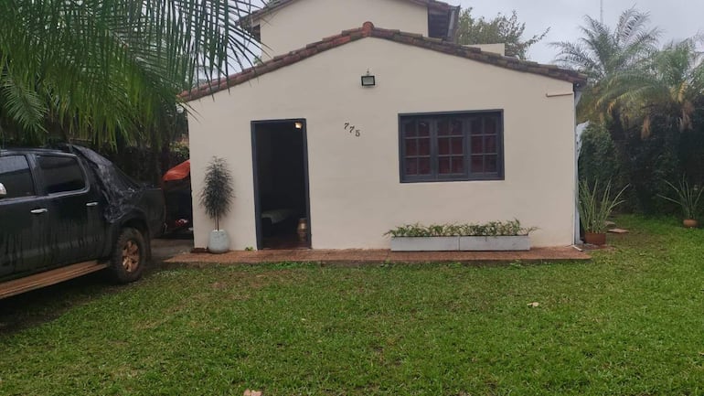 Casa de un piso con césped verde y una camioneta negra cubierta, ubicada en el barrio Santísima Trinidad.