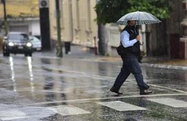 Un ciudadano cruza la calle en Asunción, que está cubierta de agua, con una sombrilla para protegerse de las precipitaciones.