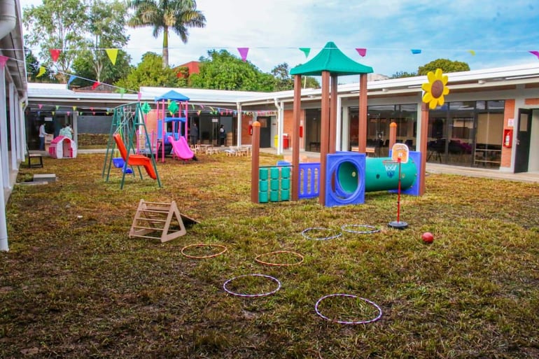 Área de recreo al aire libre con toboganes rosas y juegos de baloncesto, decorado con banderines de colores.