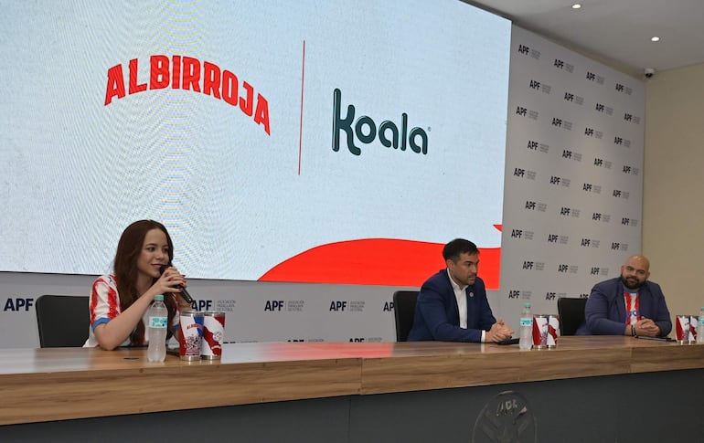Mujer con vestimenta de selección paraguaya y hombre con chaqueta azul en evento formal de Koala y la APF, con logo de Albirroja visible.