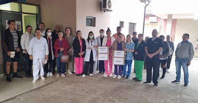 Grupo de médicos y enfermeras con batas coloridas sosteniendo carteles que dicen 'PRESENTES EN LA LUCHA'.