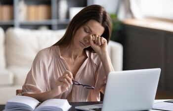 Una mujer preocupada se refriega la vista frente a una computadora