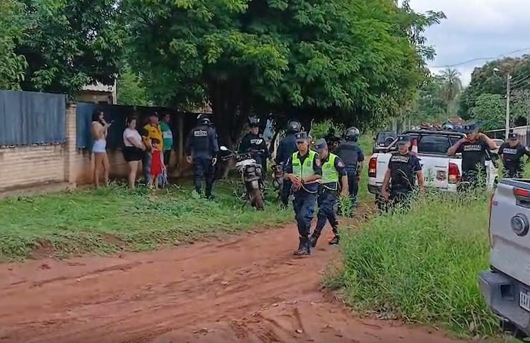 Agentes policiales en uniforme negro se comunican mientras dos mujeres observan de pie en un entorno de tierra y vegetación.