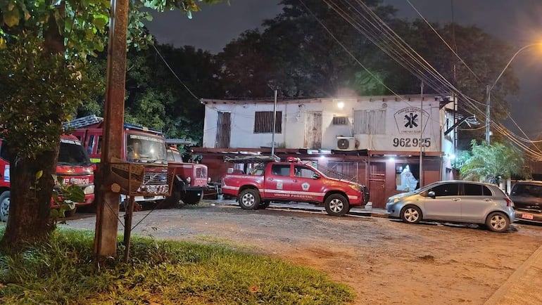 Camiones de bomberos y camioneta 'Unidad Forestal' estacionados frente a edificio iluminado por farolas.