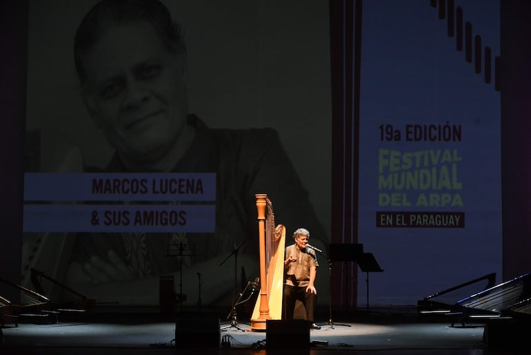 Marcos Lucena en escenario con cabello rizado y vestimenta colorida, interactuando con el público en el festival del arpa.