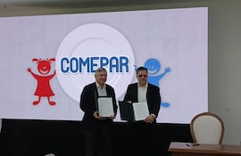 Dos hombres, uno con chaqueta oscura y camisa blanca, firman documentos ante un gran panel del programa COMEPAR.