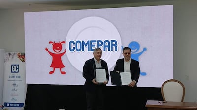 Dos hombres, uno con chaqueta oscura y camisa blanca, firman documentos ante un gran panel del programa COMEPAR.