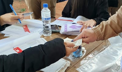 Personas en un centro de votación, con documentos y agua mineral en la mesa. Ambiente activo y de intercambio.