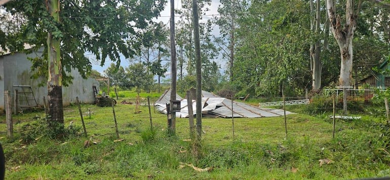 Área rural con trozo de techo metálico en el suelo, cercas de madera y vegetación verde abundante.