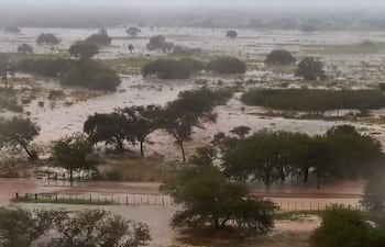 Paisaje inundado con agua cubriendo caminos y vegetación en un ambiente nuboso y lluvioso.