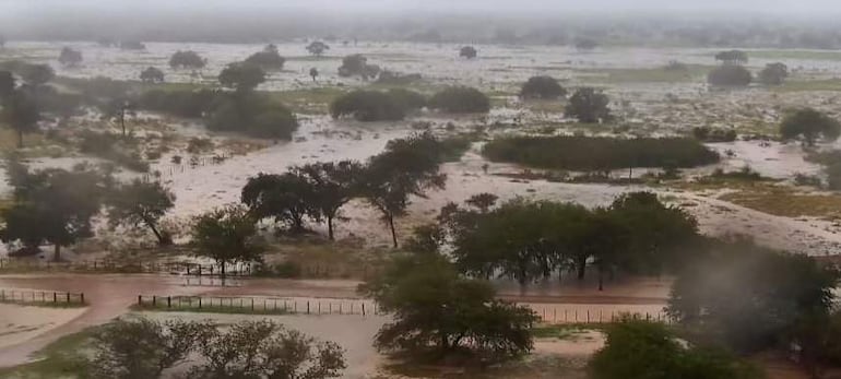 Paisaje inundado con agua cubriendo caminos y vegetación en un ambiente nuboso y lluvioso.