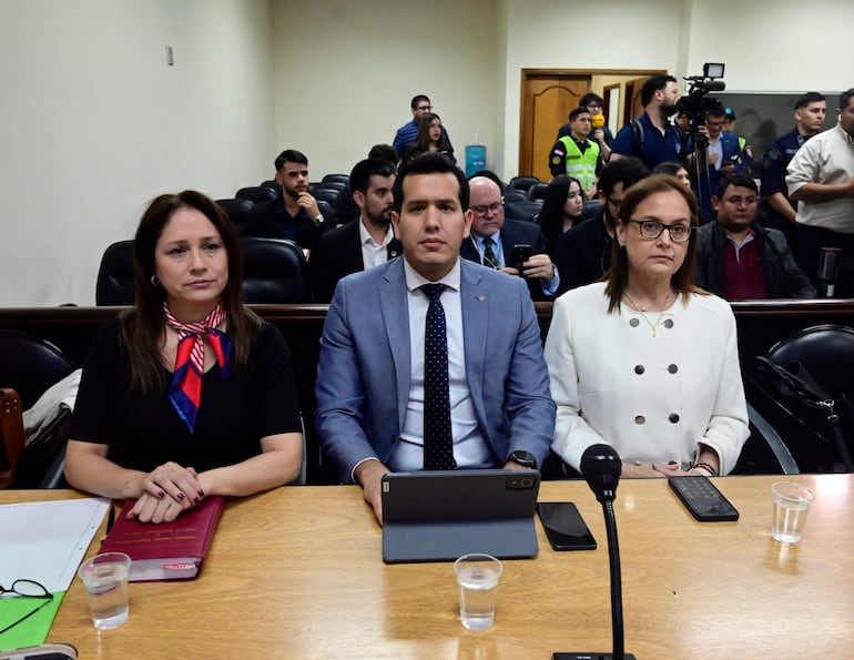 Christian Benítez con traje claro y Patricia Sánchez con abrigo blanco, ambos atentos en un ambiente formal.